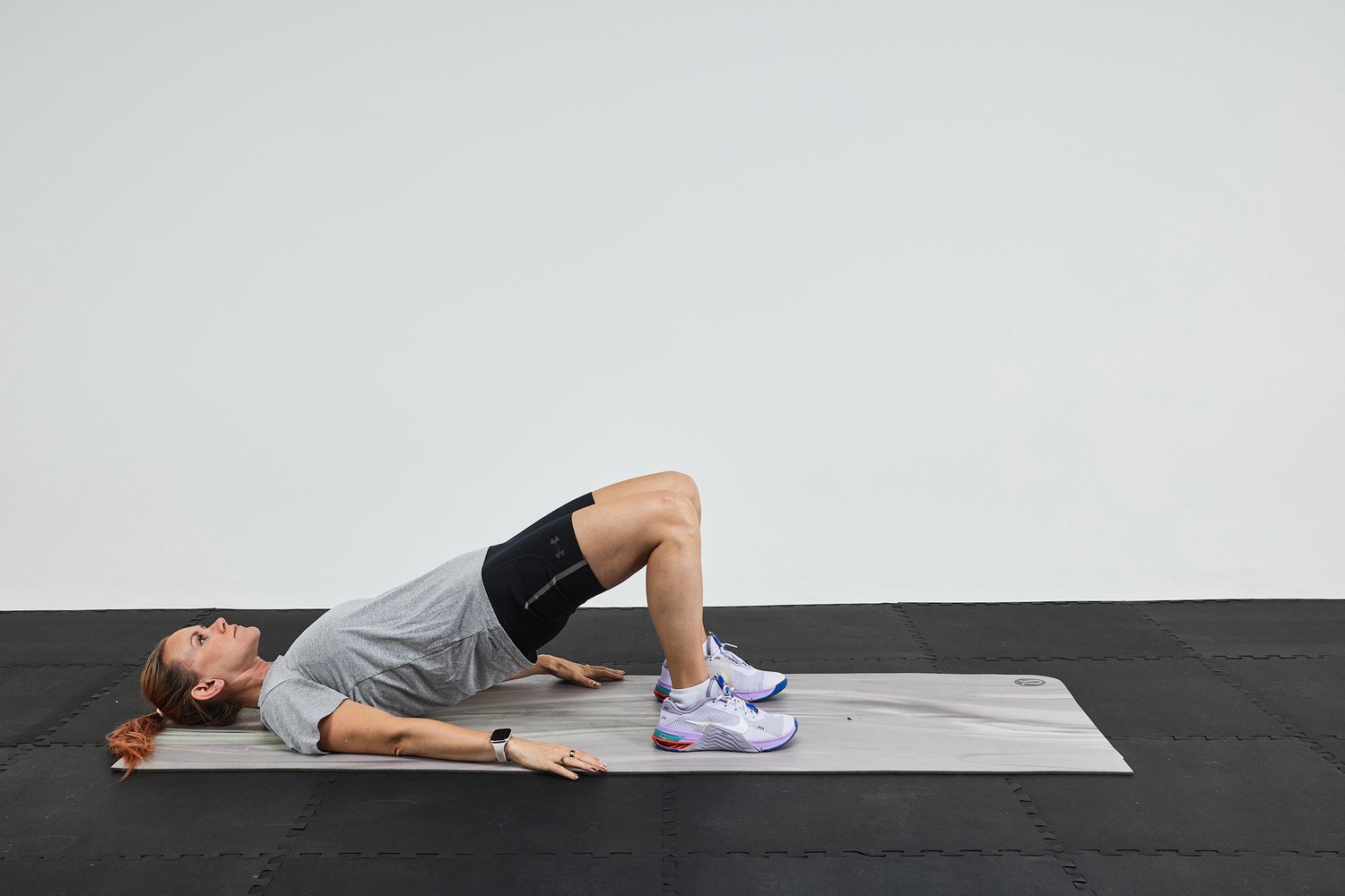 Person performing a bridge exercise on an exercise mat with a gray background.