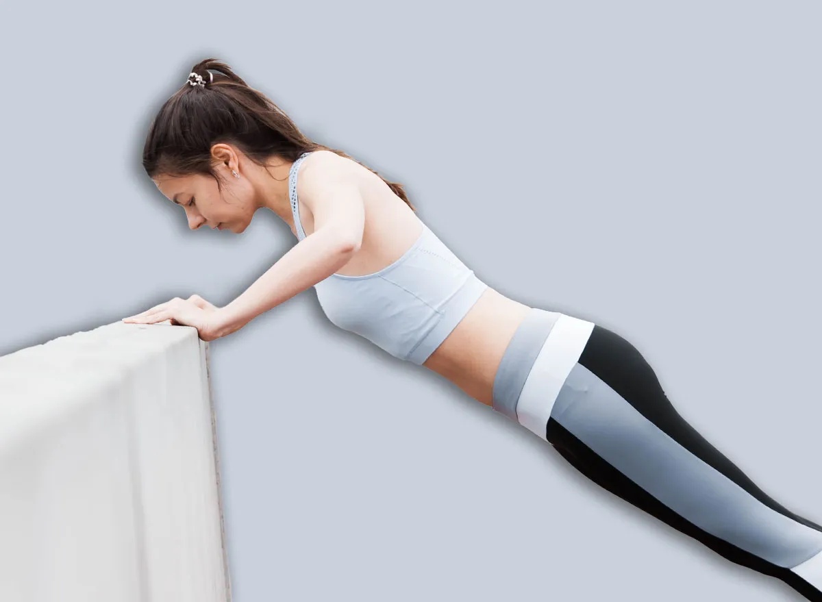 A young sports woman in a fitness suit is pushing up from the curb, parapet of the bridge, against the backdrop of an urban cityscape. Copyspace.