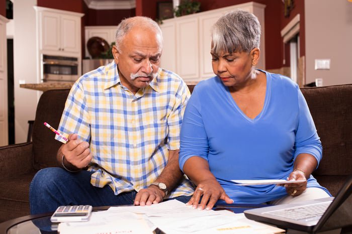 A couple is sitting on a couch, reviewing bills and financial statements set on a table in front of them.