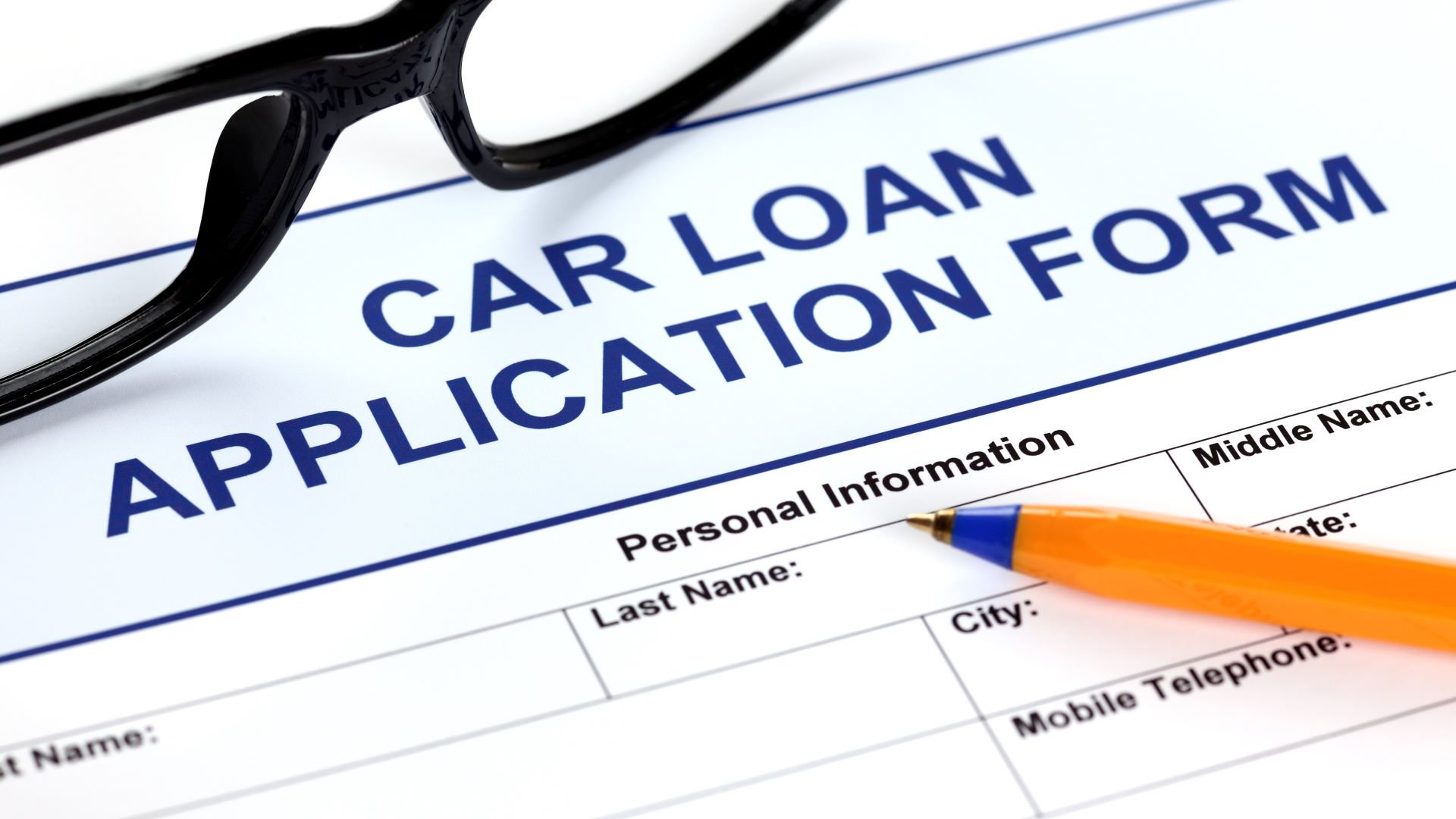 Discover a close-up of a car loan application form with eyeglasses and an orange pen resting on top