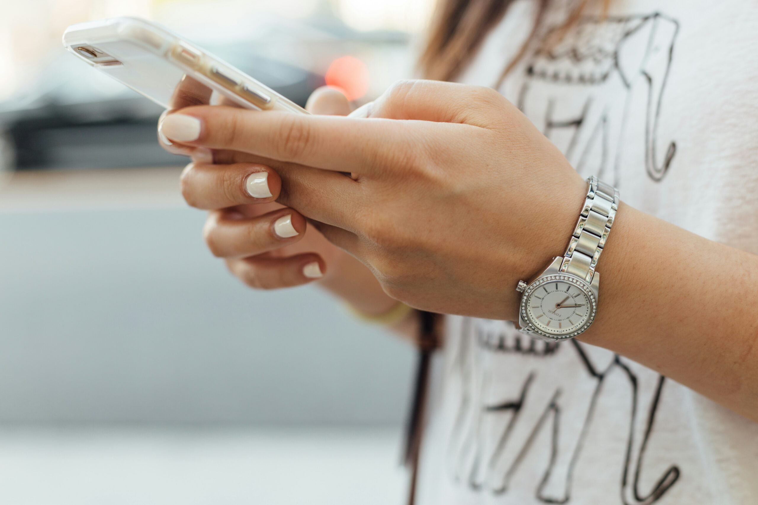 A person holding a smartphone with both hands, wearing a silver watch on their wrist.