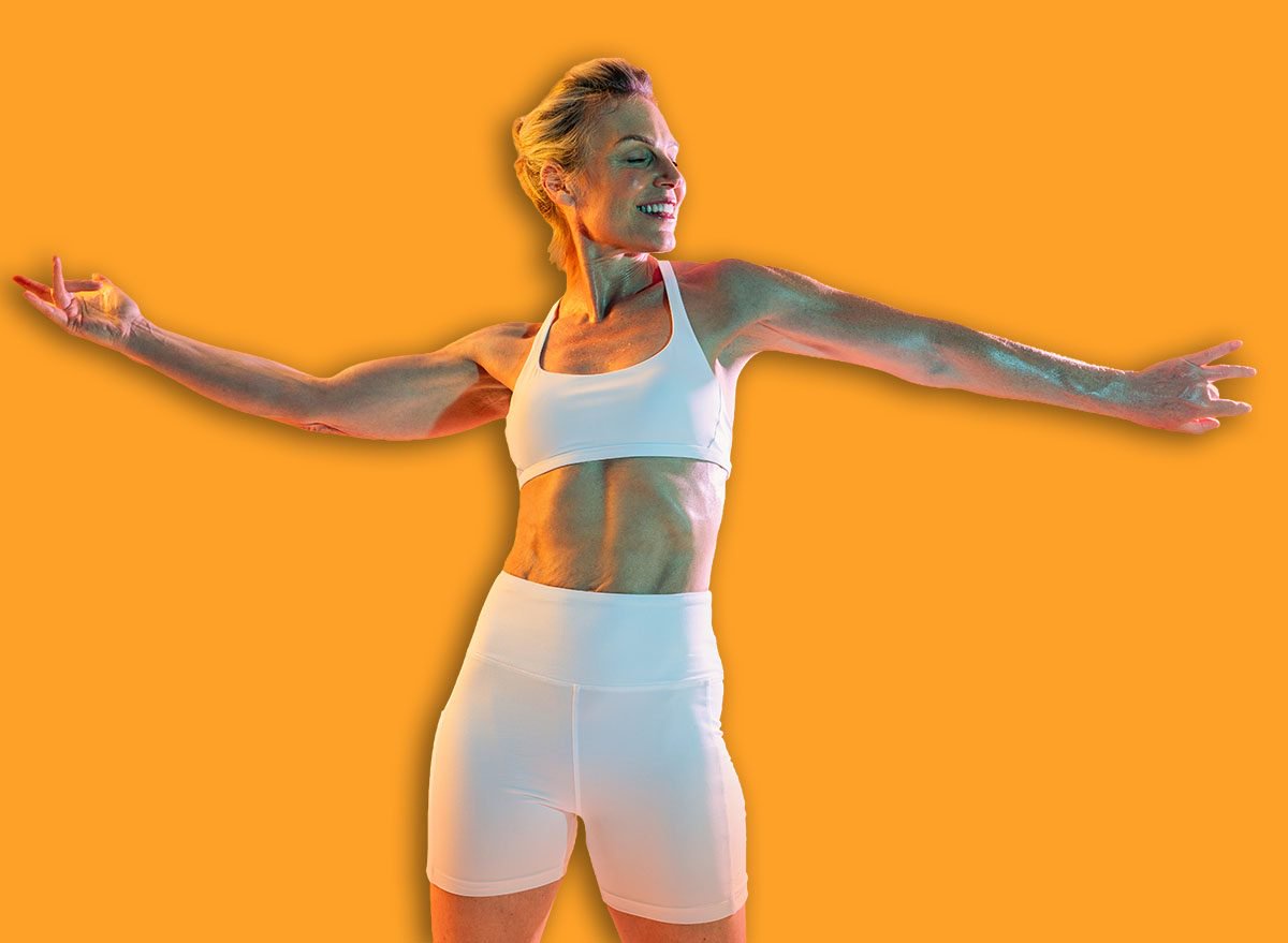 Beautiful mature sportive woman wearing sportswear doing workout - fit, mature woman in sportswear dynamically stretching against a vibrant orange backdrop, embodying strength and flexibility