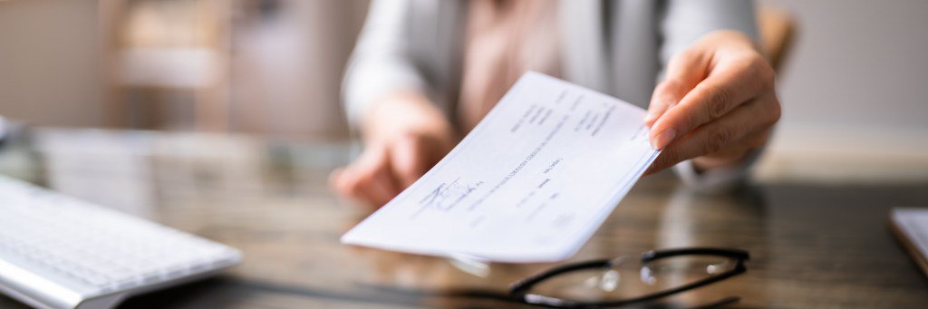 Close-up of a businessperson's hand holding a cheque in an office.