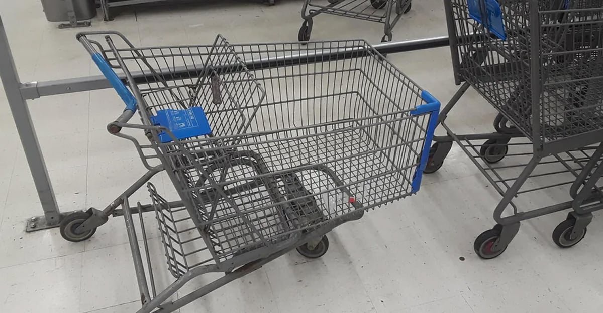 A broken shopping cart with a collapsed front end is positioned next to two normal shopping carts inside a store on a white tiled floor.