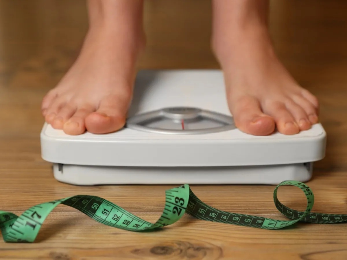 Stock image: someone stands on scales near measuring tape on a wooden floor.