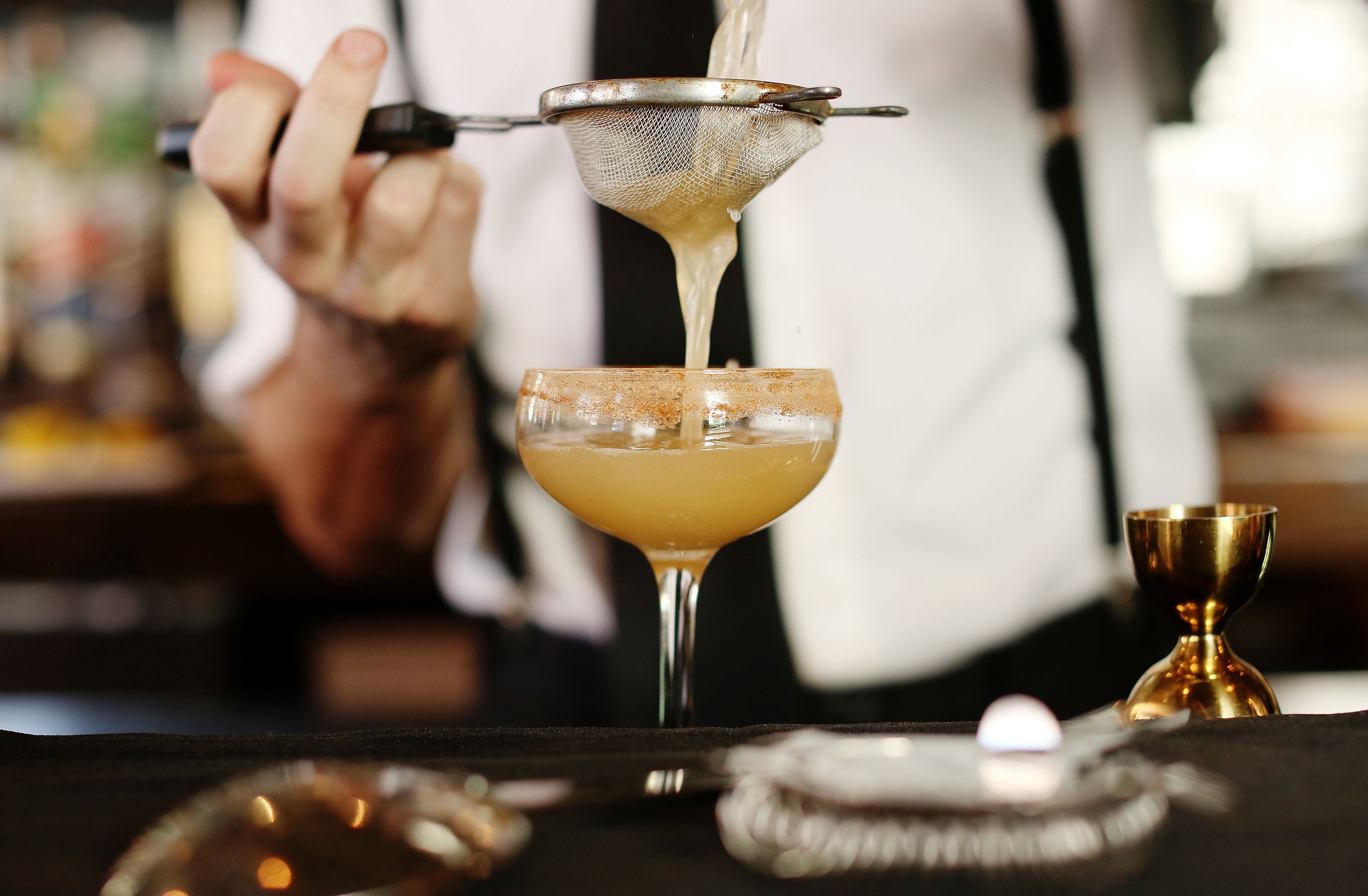 Bartender straining a mixed cocktail into a coupe glass at a bar