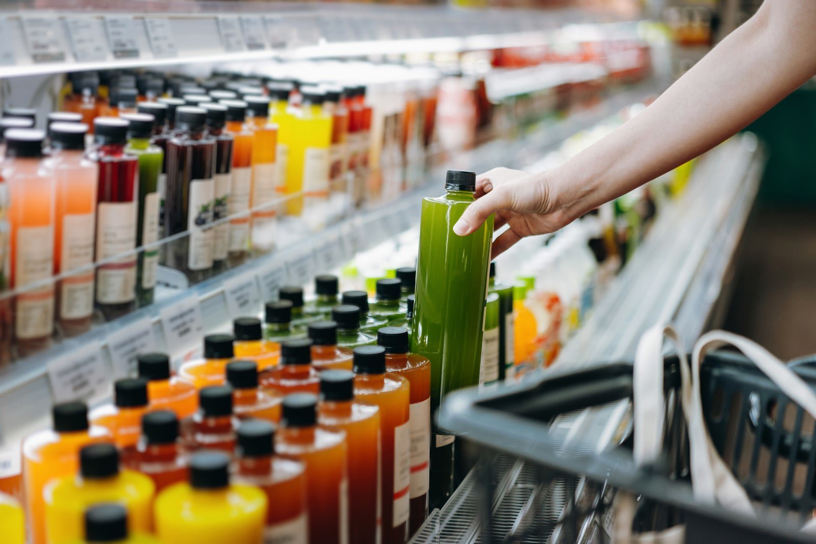 a persons hand pulling a juice bottle from a store shelf