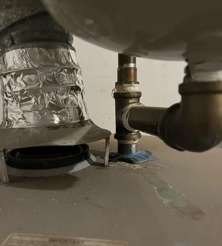 A metallic pipe connection on a water heater with a valve, showing a green stain from a blue plastic piece.