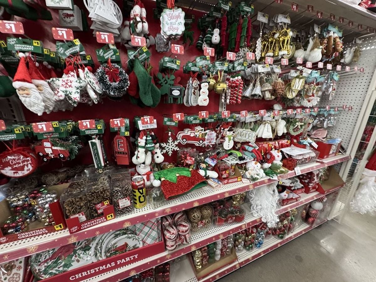 Shelves in a store display a variety of Christmas decorations, including ornaments, garlands, figurines, stockings, and festive signs, all arranged in colorful and festive holiday packaging.