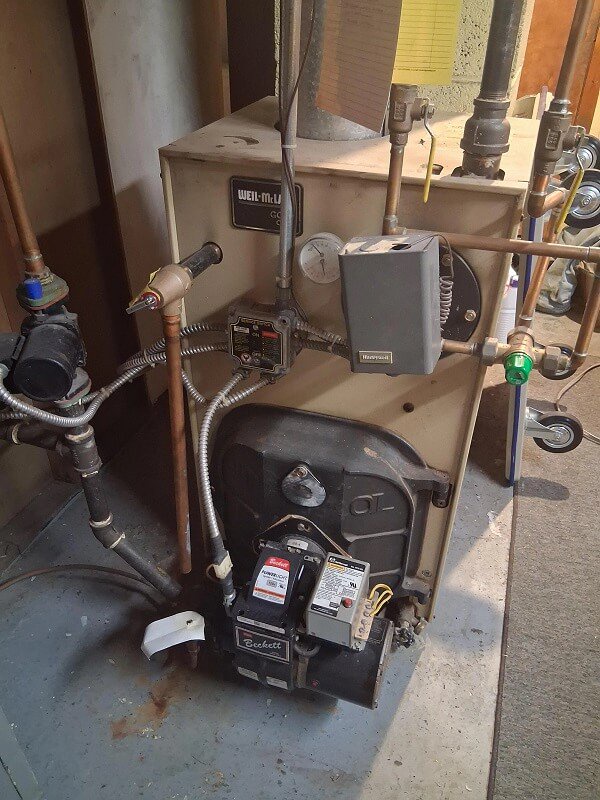 A heating system with valves, wires, and a control box in a basement setting.