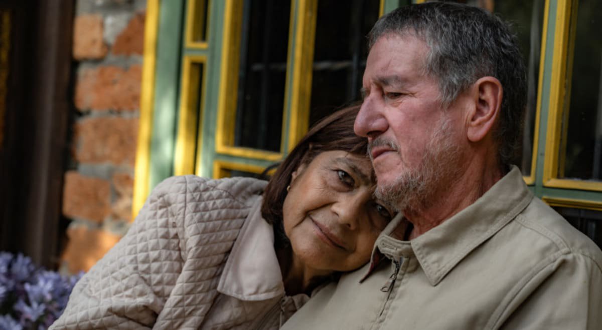An older couple lean against each other with worried eyes.