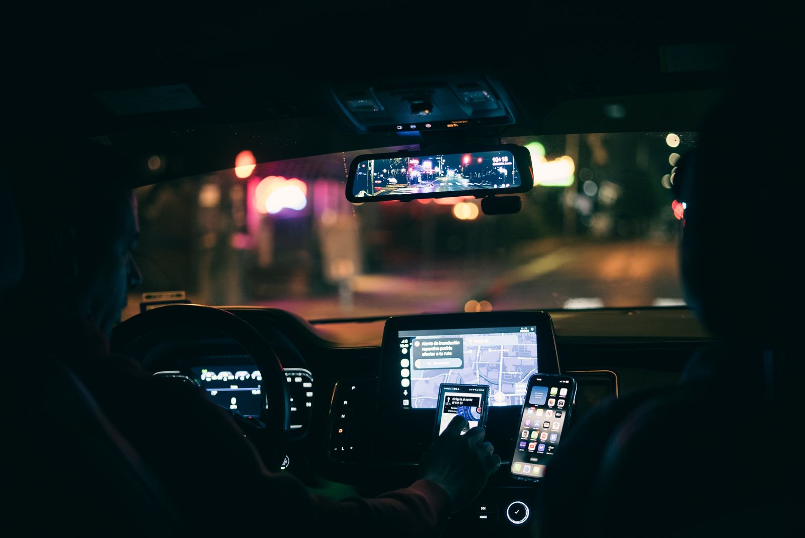 Driver at night with a phone and navigation screen lit on the dashboard