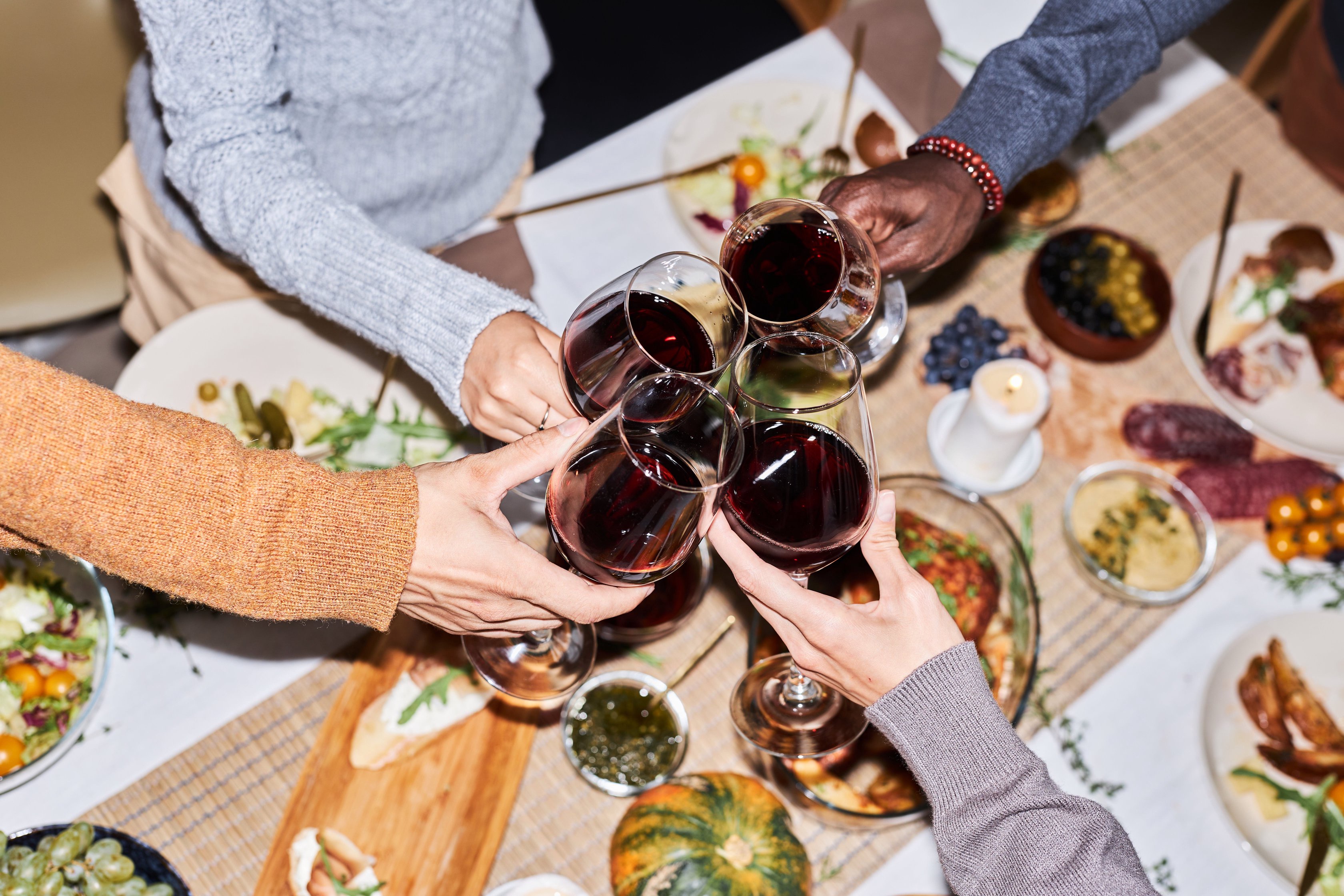 People toasting with glasses of red wine over a table filled with plates of food
