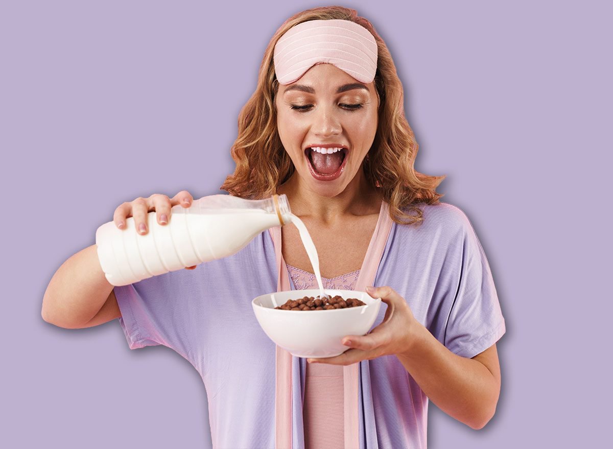 Image of caucasian cheerful woman in sleep mask smiling while making instant breakfast isolated over pink background
