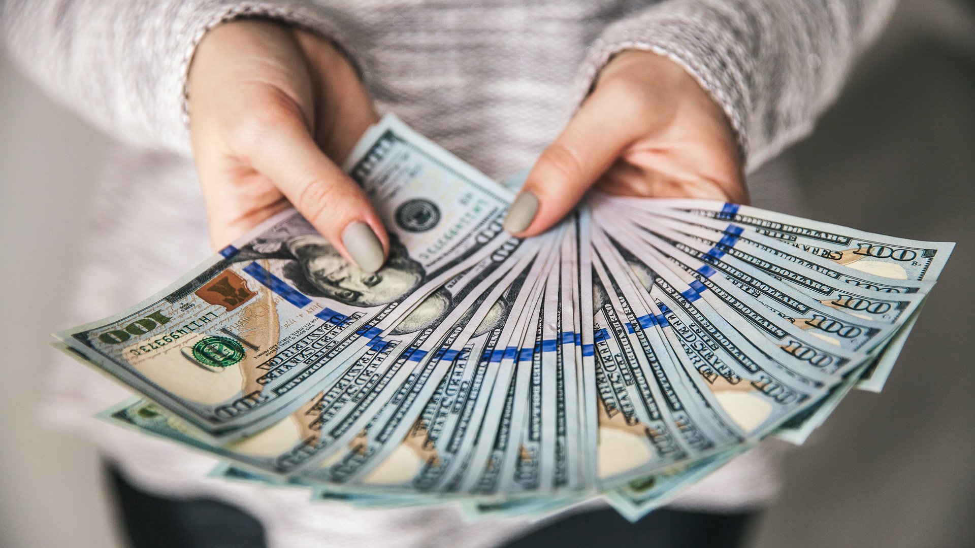 Discover a woman with painted fingernails holds on display a stack of one hundred dollar bills spread out in her hands