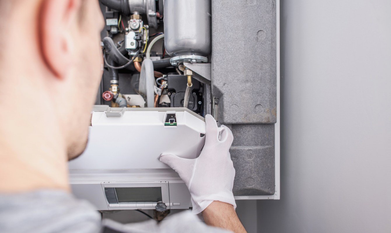 A person in gloves is working on a mechanical device inside a wall-mounted unit.