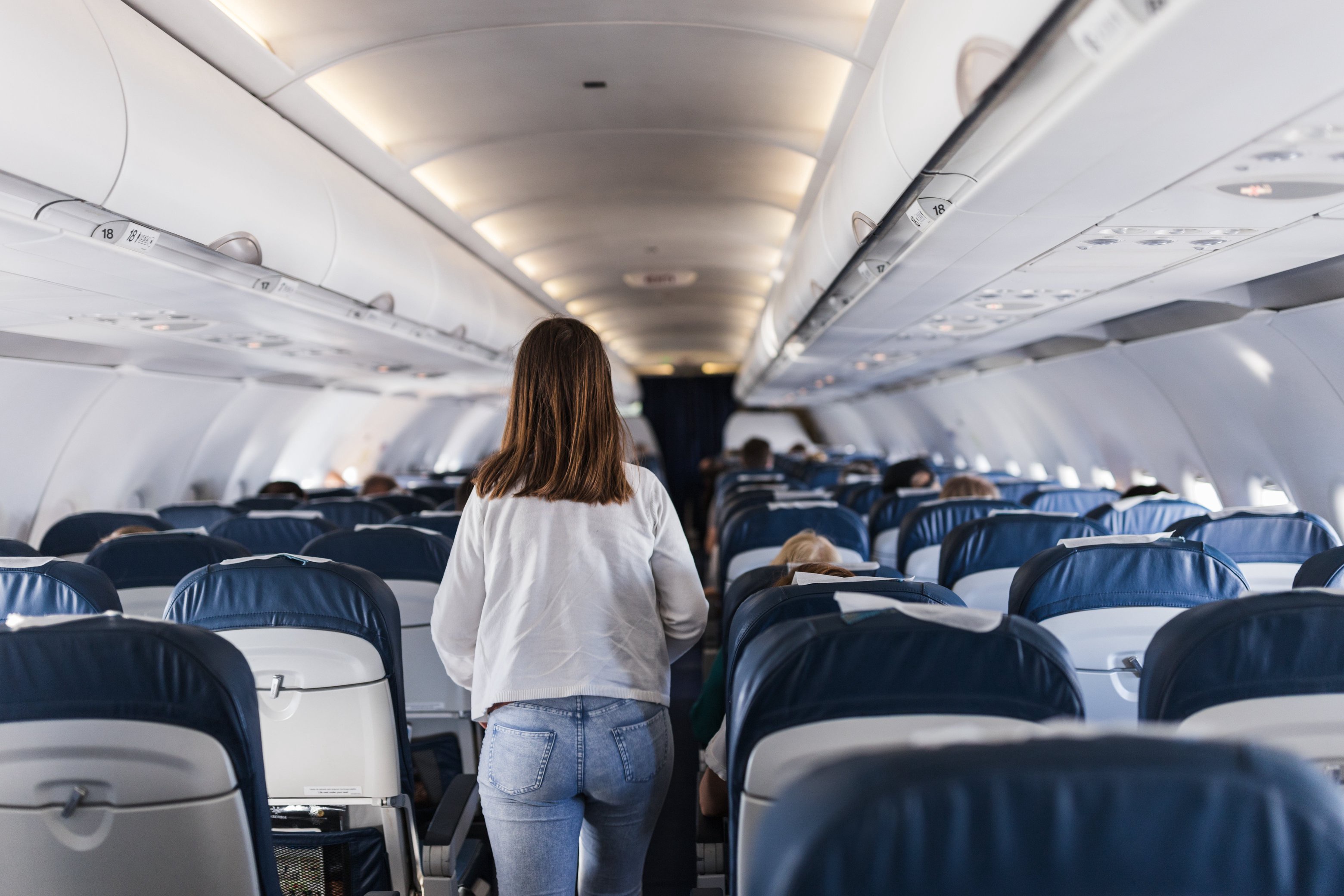 Person walking down an airplane aisle, with rows of seated passengers on both sides