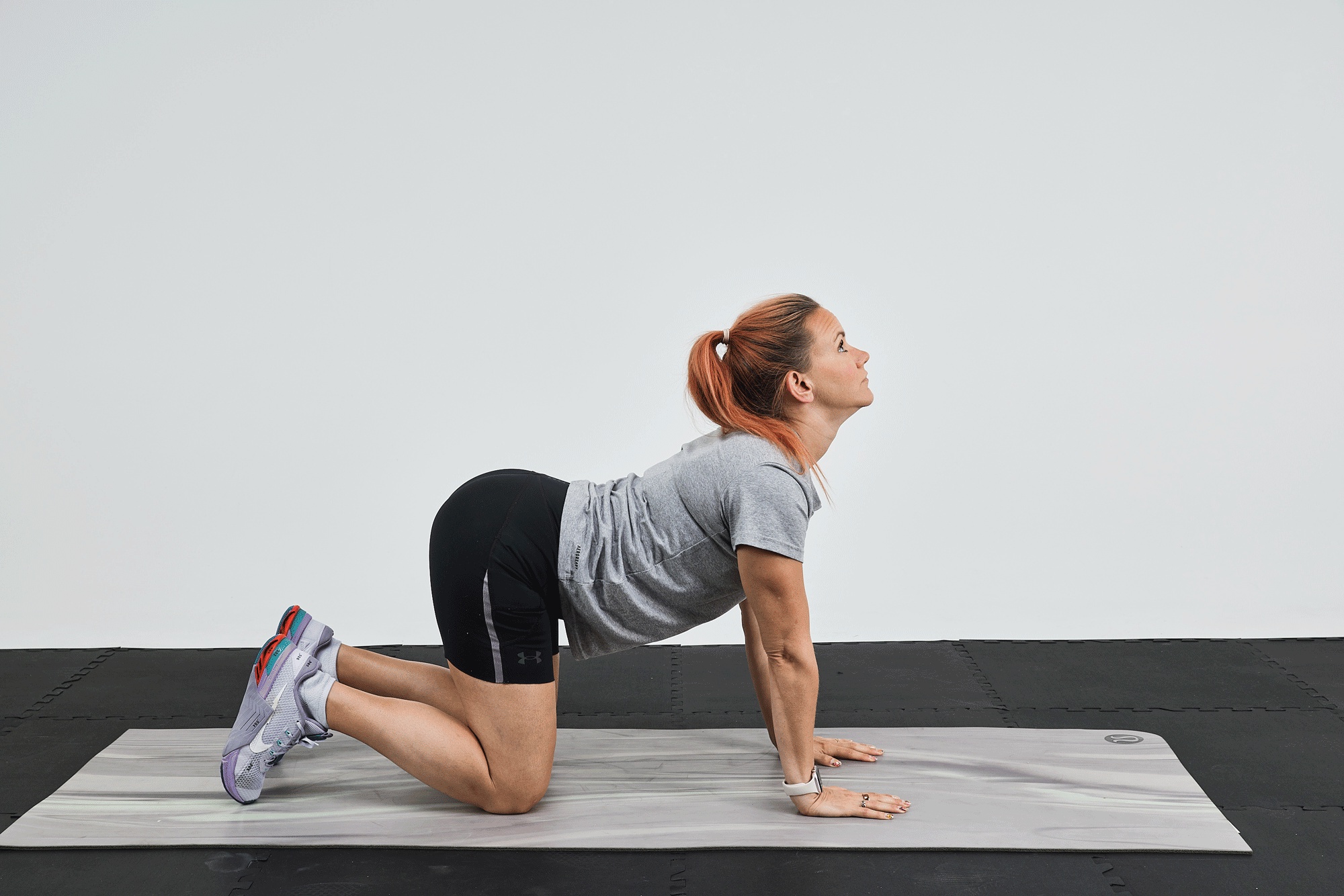 Woman performing a yoga pose on a mat, with her back arched and head tilted upward.