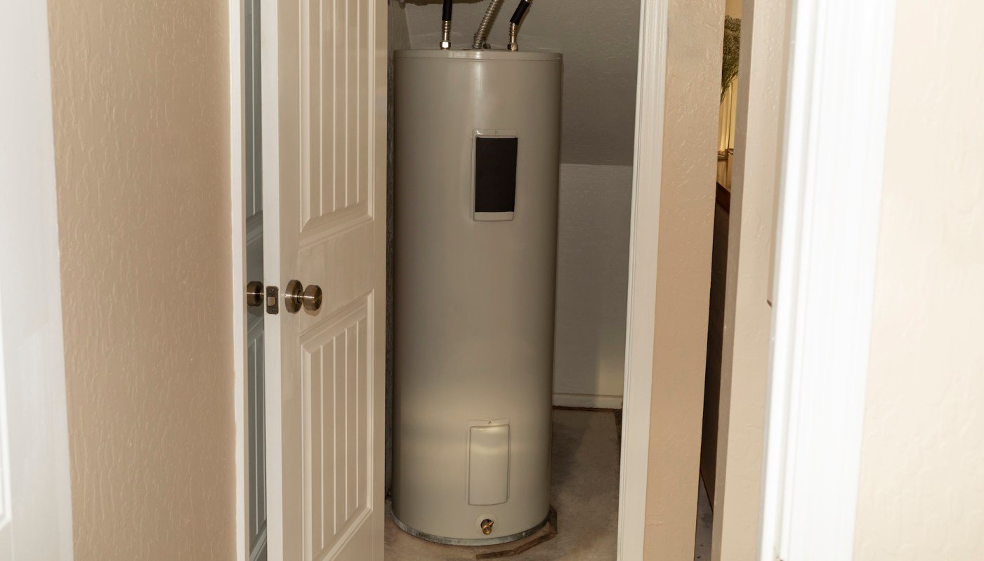 A water heater in a small, enclosed space with a door partially open.