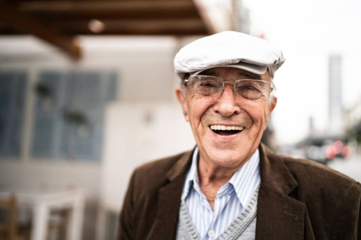 Smiling elderly man wearing glasses and a flat cap on a city street