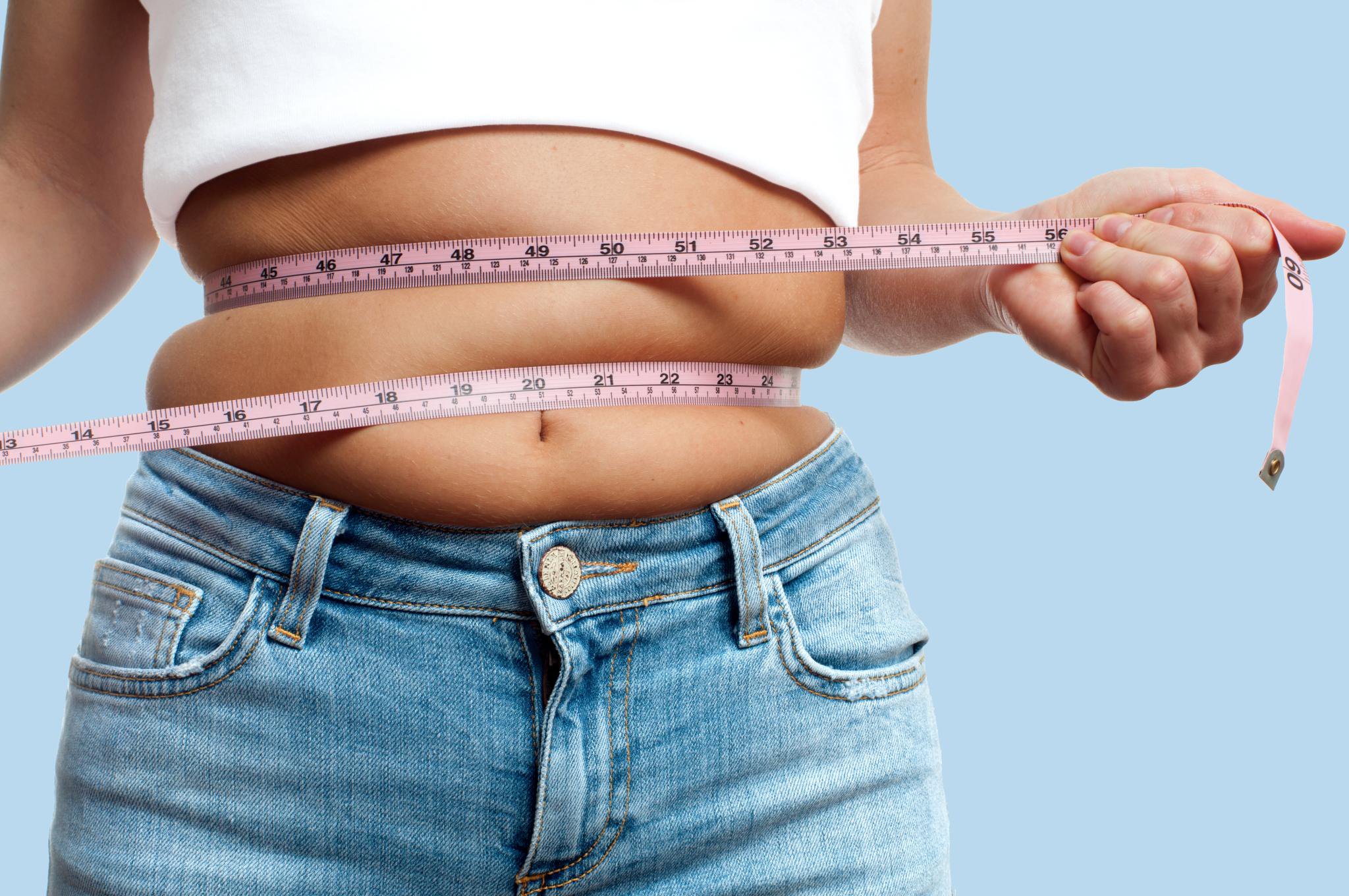 An overweight woman wraps a tape measure around her waist.