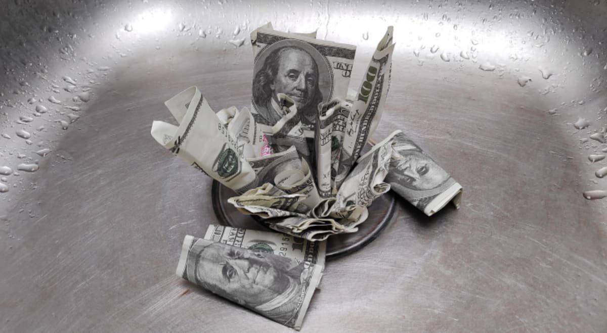 An image of hundred dollar bills clogging a wet sink drain.