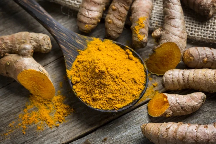Turmeric root and powder on a wooden surface.