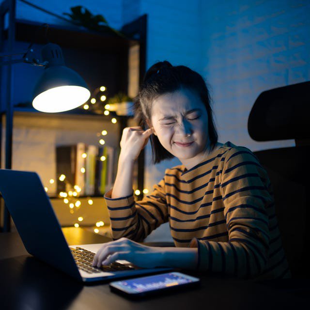 doctors explain itchy ear causes - Asian woman putting a finger into her ear and working on a laptop overtime at home. WFH. Work from home for avoid the Coronavirus COVID 19 concept.