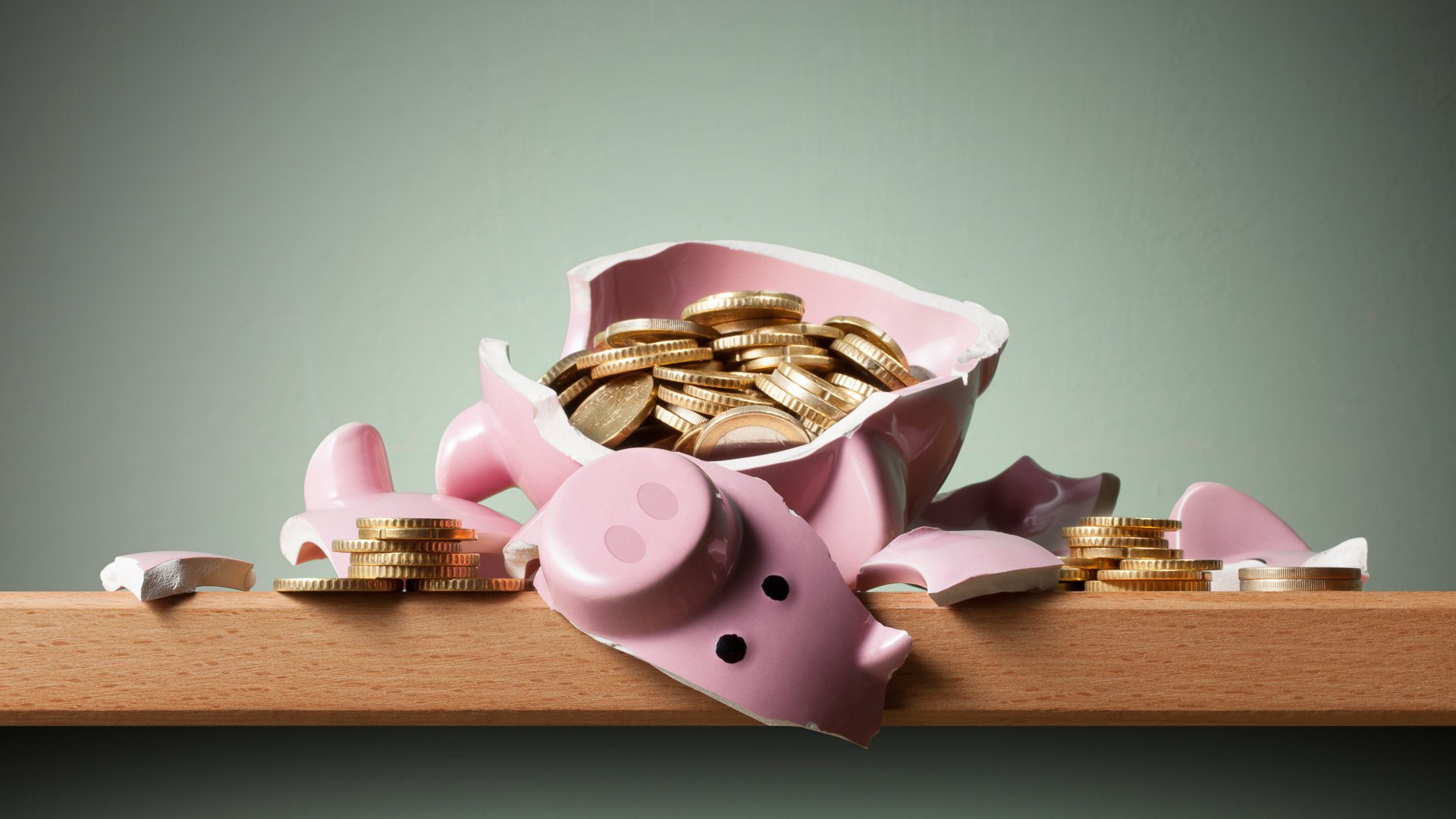 Discover a broken pink piggy bank on a shelf with gold euro coins both inside and out, symbolizing breaking into savings.