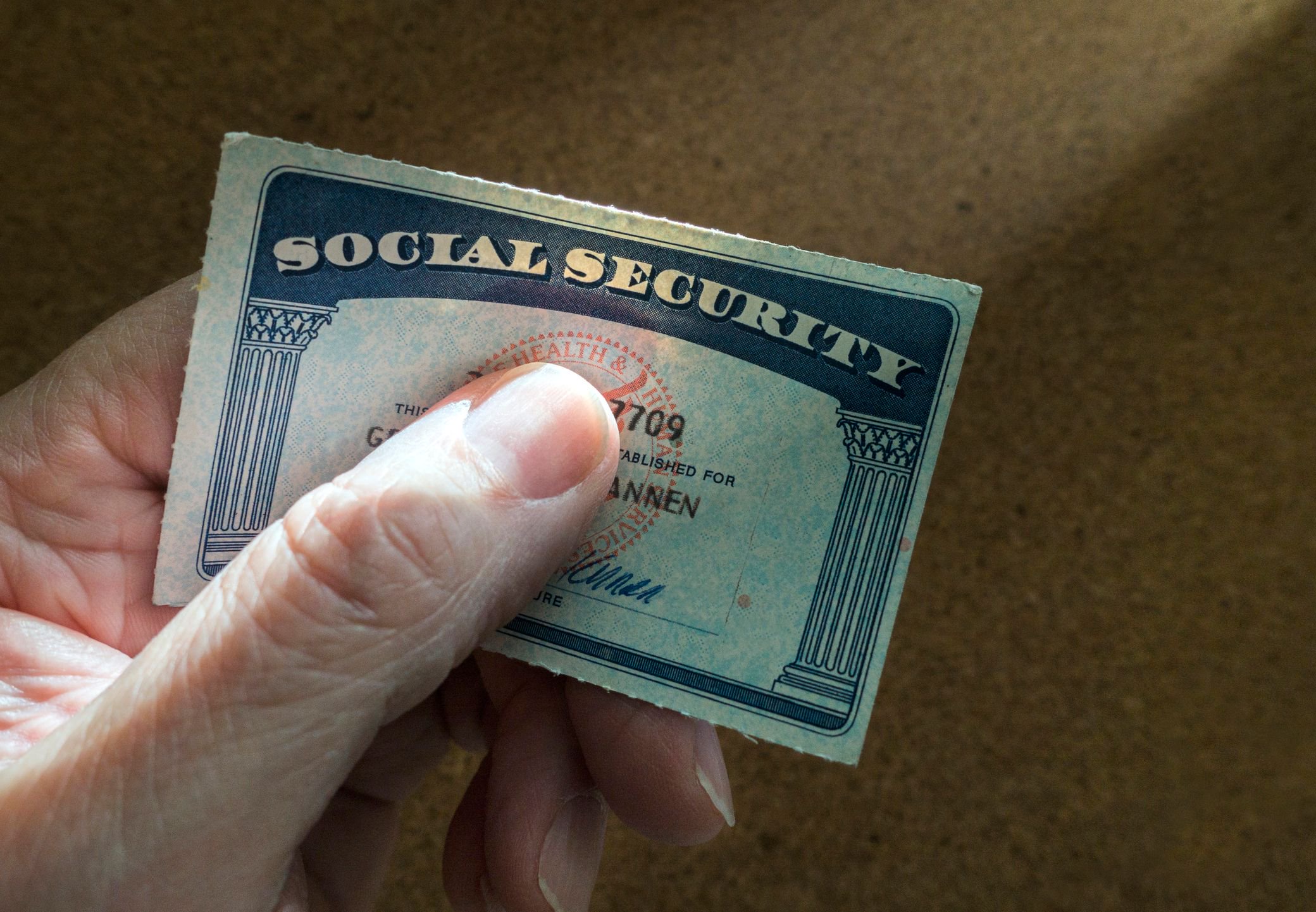 Hand holding a U.S. Social Security card against a plain brown background