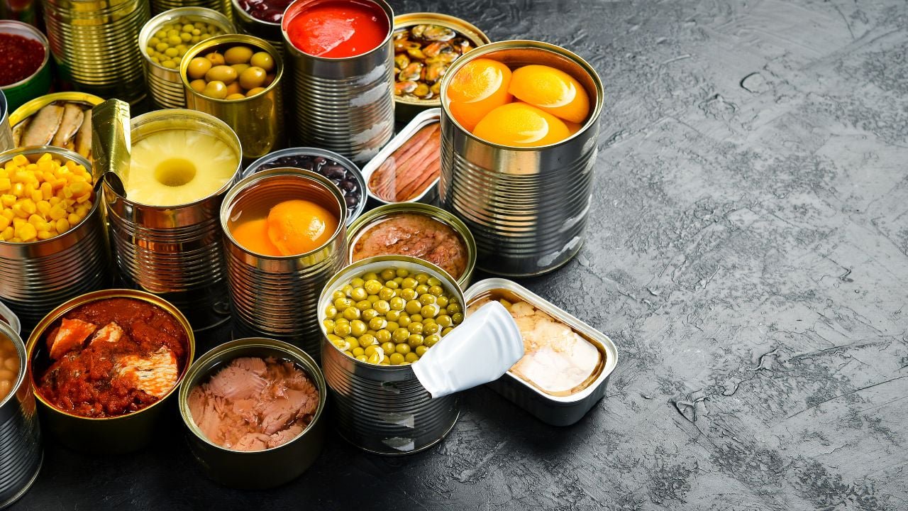 Assortment of canned preserves food in tin open cans: fish, beans, vegetables and fruits. Food stocks. Side view.