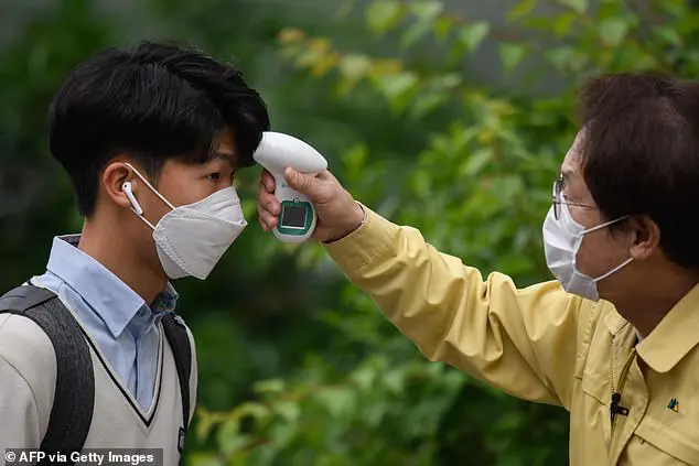 Students wearing facemasks amid concerns over coronavirus undergo a temperature check from city education officials as they arrive at Kyungbock High School in Seoul on May 20, 2020