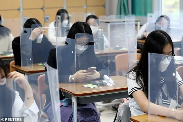High school students wearing face masks prepare for classes, with plastic covers placed on desks to prevent infection in Daejeon, South Korea, May 20, 2020