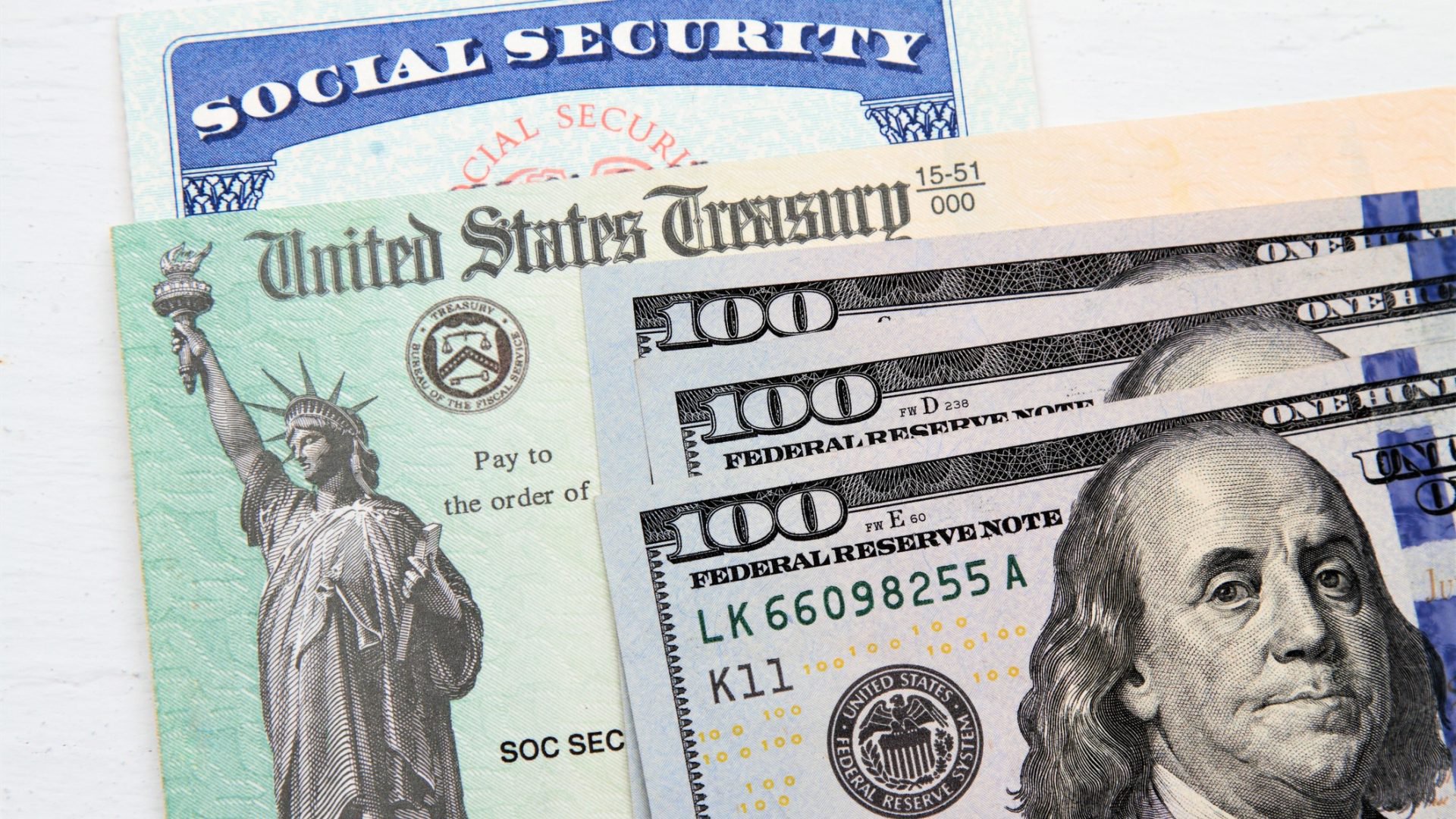 Discover a partial view of a Social Security card, US Treasury checks and hundred dollar bills on top