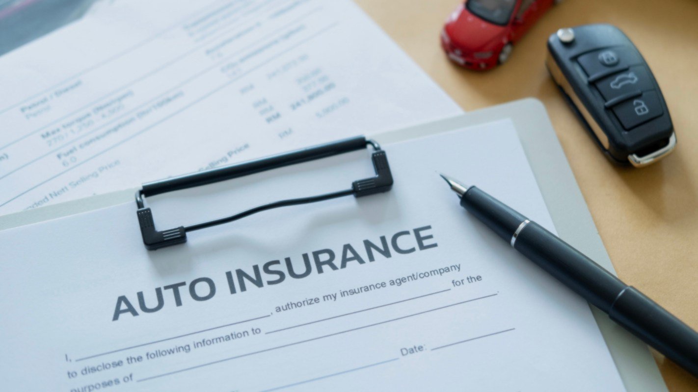 An auto insurance form is placed on a table next to a car key and a toy car.