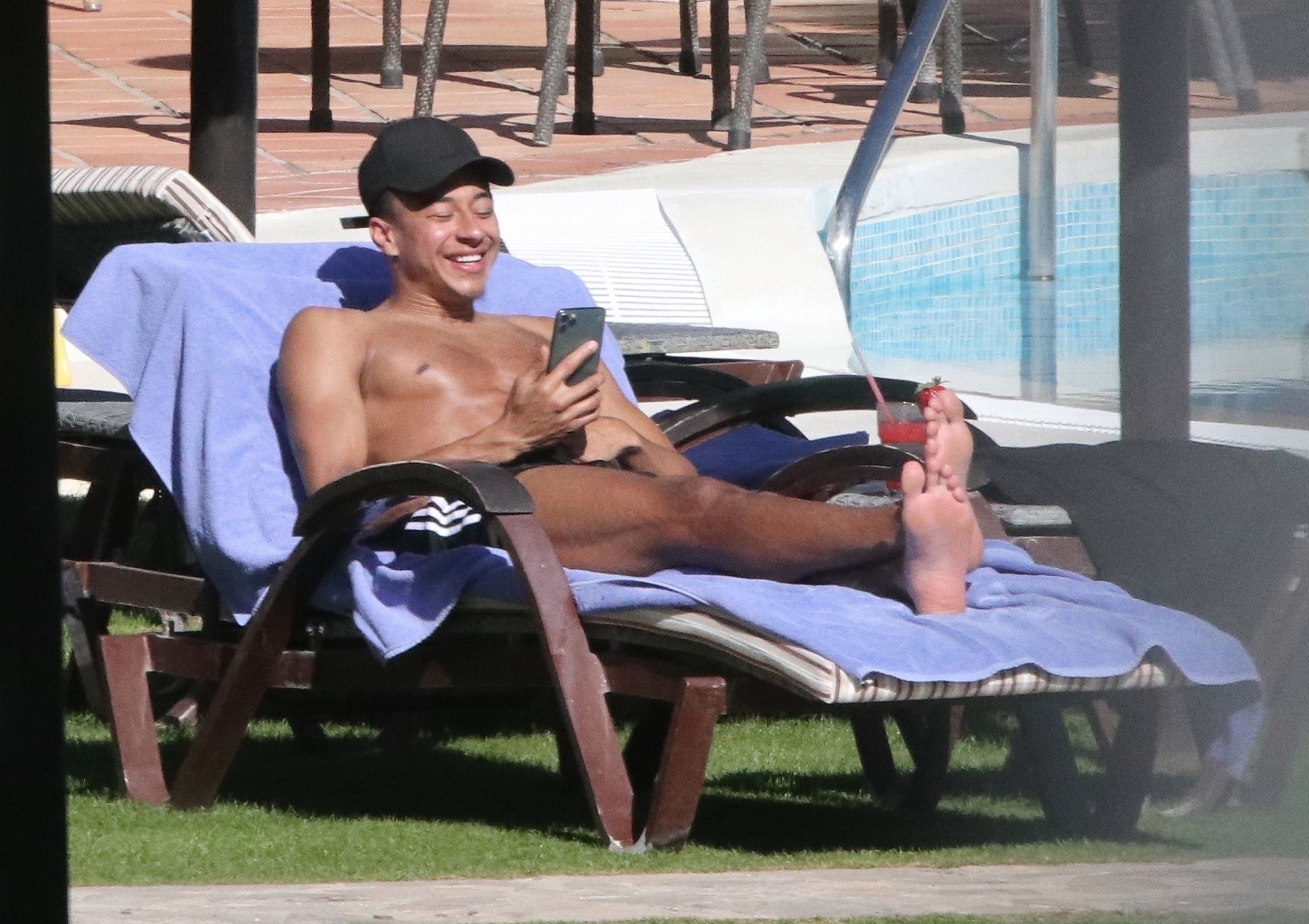  Jesse Lingard grinned as he scrolled down his phone while chilling on a sun lounger