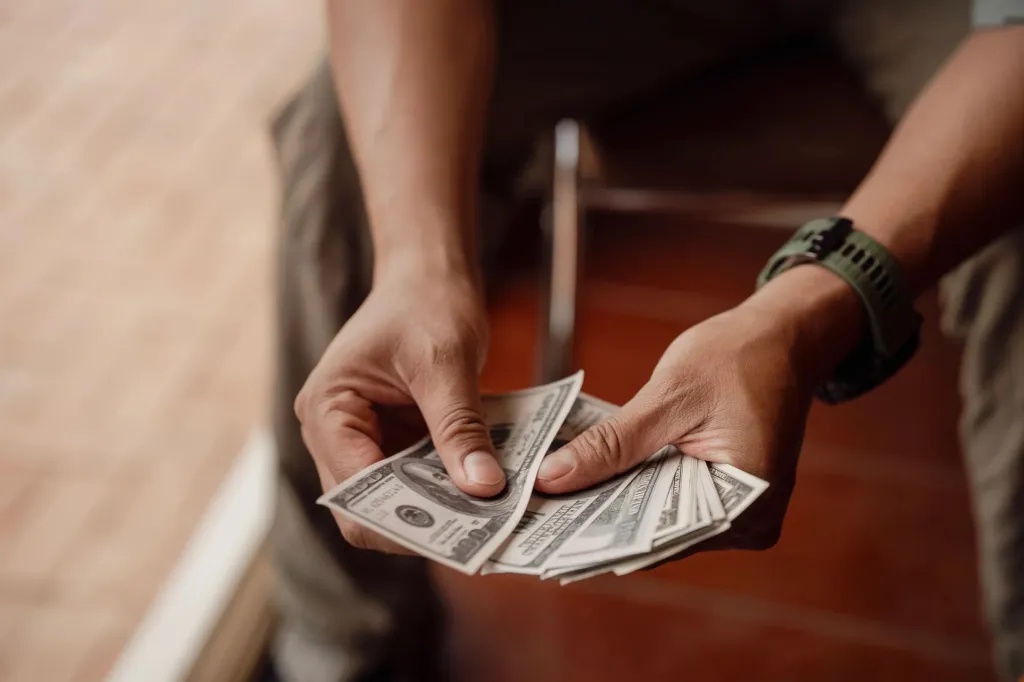 An image collage containing 1 images, Image 1 shows Person Holding and Counting US Dollar Bills