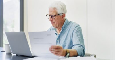 Documents, laptop and research with old man in home for retirement fund, asset management and credit score. Contact, online banking and pension account report with senior person in apartment