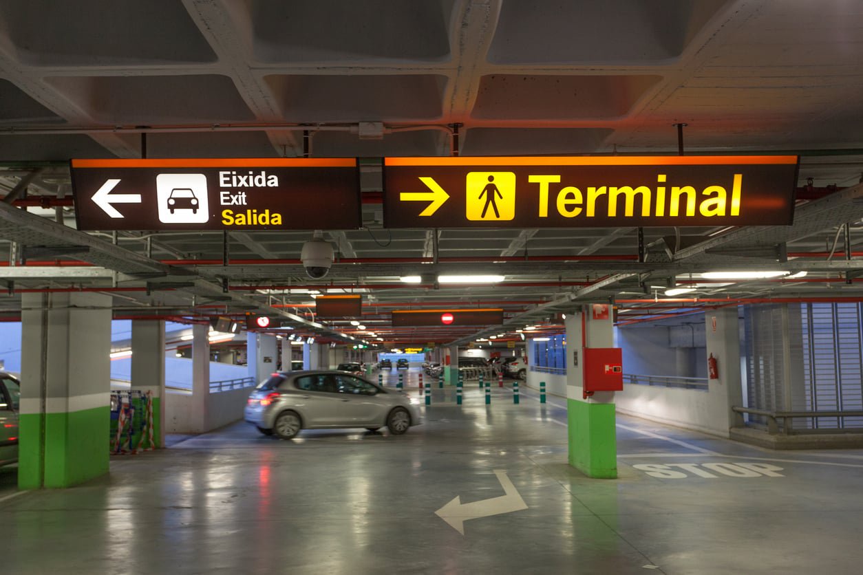 Overhead parking garage signs directing to the exit and terminal, with a car driving through the lane below.