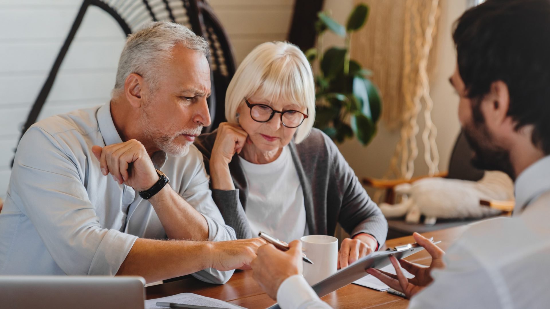 Discover Financial advisor explaining paperwork on a tablet to elderly retired couple front of desk.