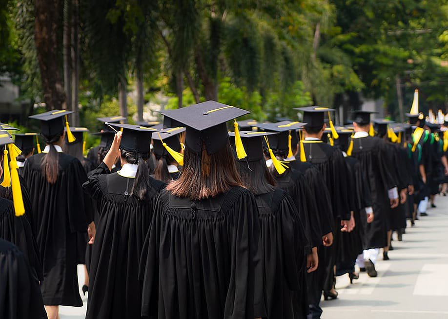 University graduates in black toga gowns lining up for their graduation ceremony. — PrasitRodphan // Shutterstock