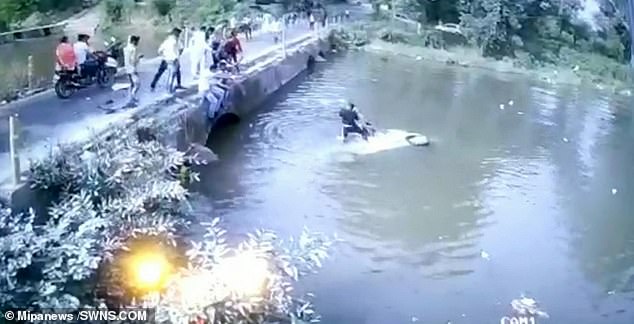 A driver's head pokes out the window as he struggles to get one child out. He then stands on the bonnet as he throws his child towards the bridge