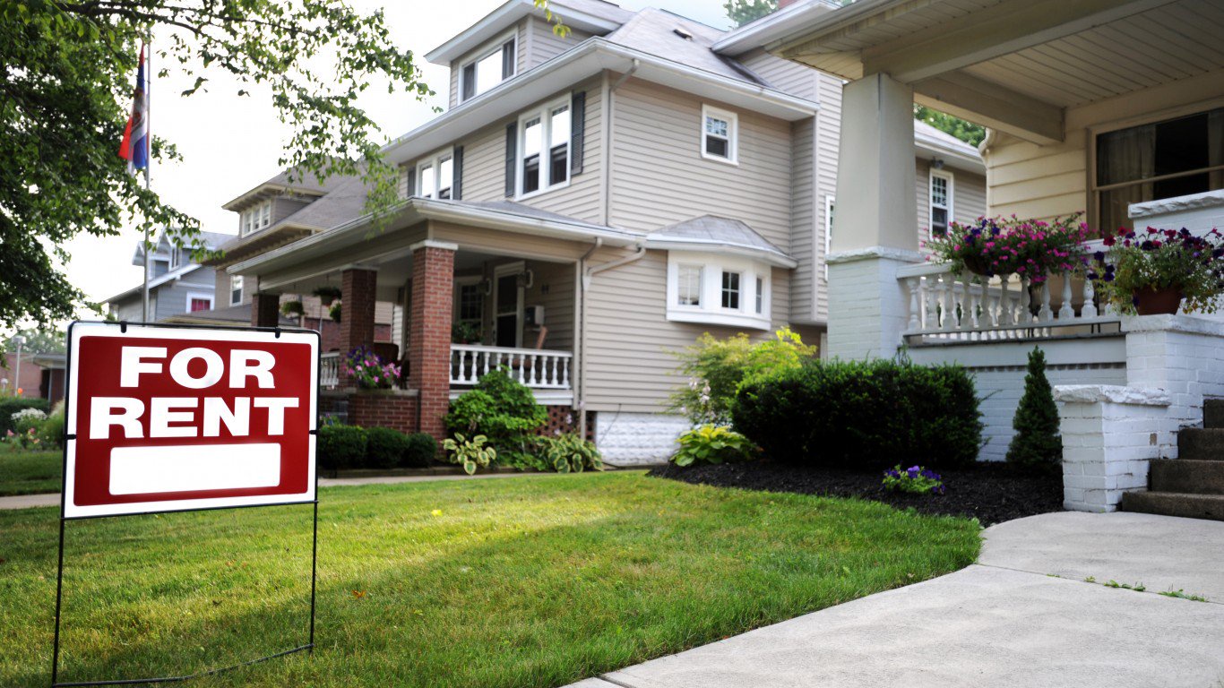 A red 'For Rent' yard sign standing on the front lawn
