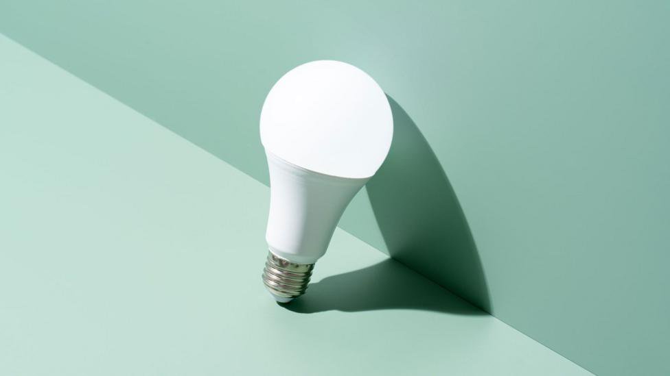An LED lightbulb leaning against a wall. the surface and wall are both duck egg blue but the wall is a darker tone. 