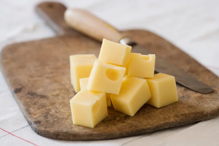 Cubes of cheese on a cutting board with a knife in the background