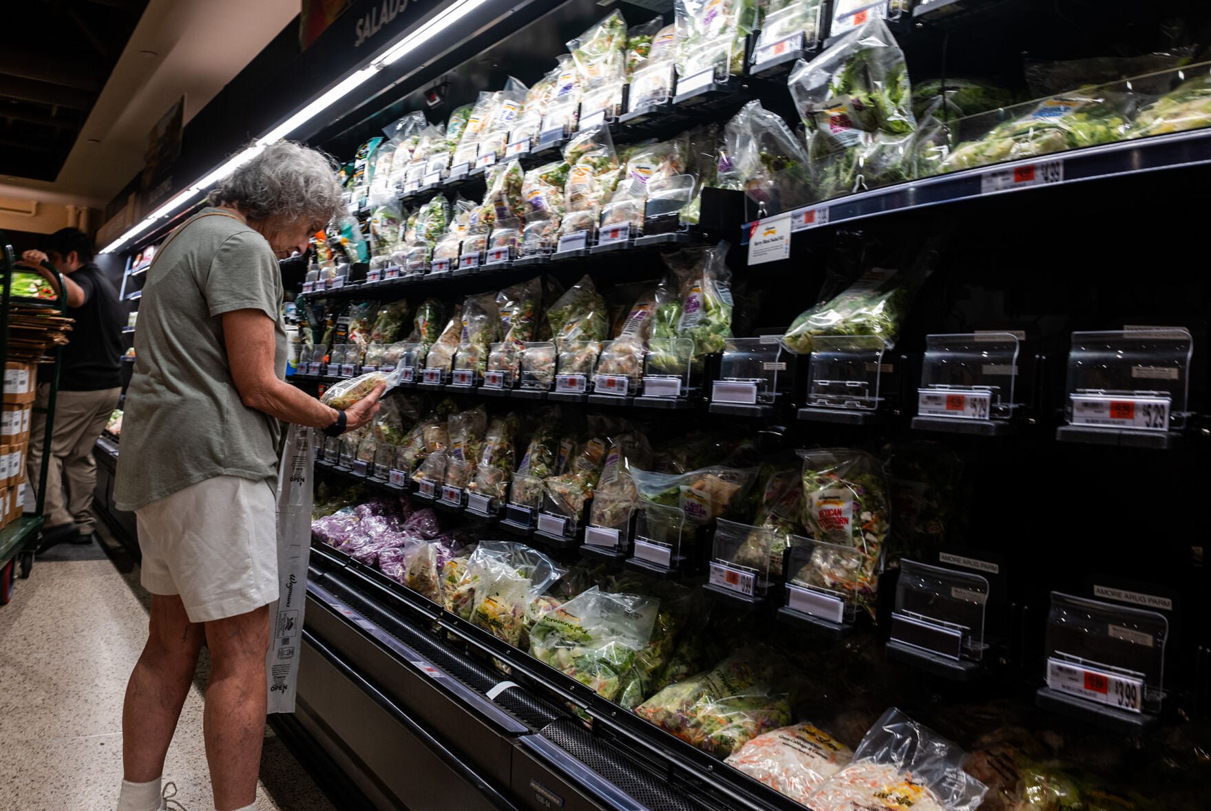 A customer examines salad and lettuce displayed on the shelf of a Manhattan grocery store on Aug. 13, 2026, in New York City.