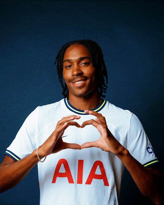 Djed Spence makes a love heart symbol with his hands in front of a blue backdrop