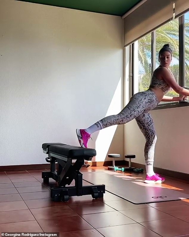 Looking good: Georgina's snakeprint leggings and matching sports bra showed off her toned abs and pert posterior as she complete the exercise while enjoying the view outside