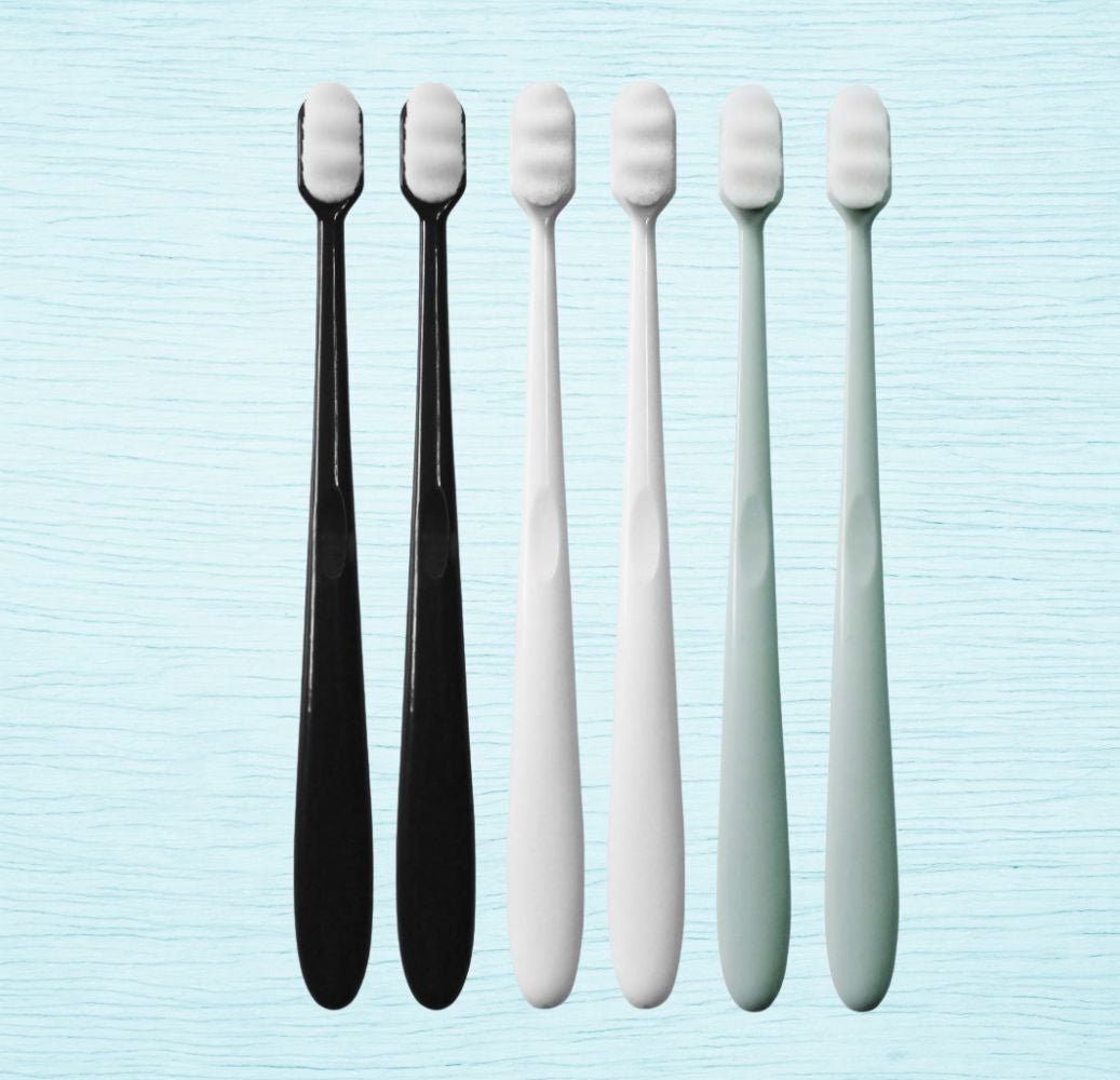 Five toothbrushes with soft bristle heads, three in white and two in black, displayed vertically on a textured background