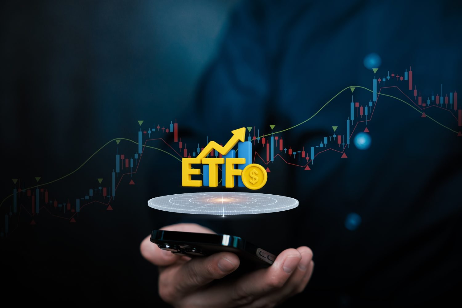 A close-up of a person's hand holding a black smartphone, from which a glowing, holographic projection emanates. The projection displays large yellow letters 'ETF', a prominent yellow upward-pointing arrow, and blue bar charts. To the right of the letters is a gold coin embossed with a dollar sign. In the blurred, dark blue background, a stock market candlestick chart with red and blue bars, along with green and red trend lines, is visible. The scene evokes digital finance and investment strategy.